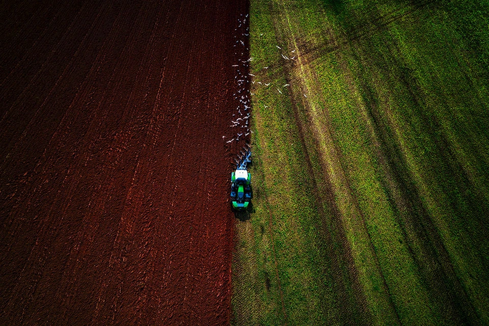 Aerial image of a tractor ploughing a field with green on the right and brown on the left.